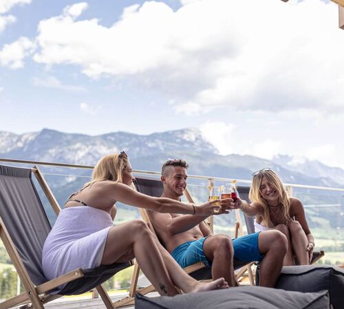 3 Freunde sitzen auf der Terrasse ihres Chalets und stoßen auf ihren Urlaub an.