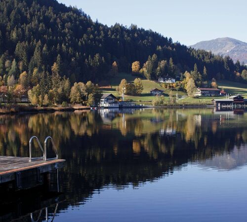 Ein stiller Bergsee in Tirol spiegelt am frühen Morgen die umliegenden Wälder und majestätischen Gipfel im klaren Wasser