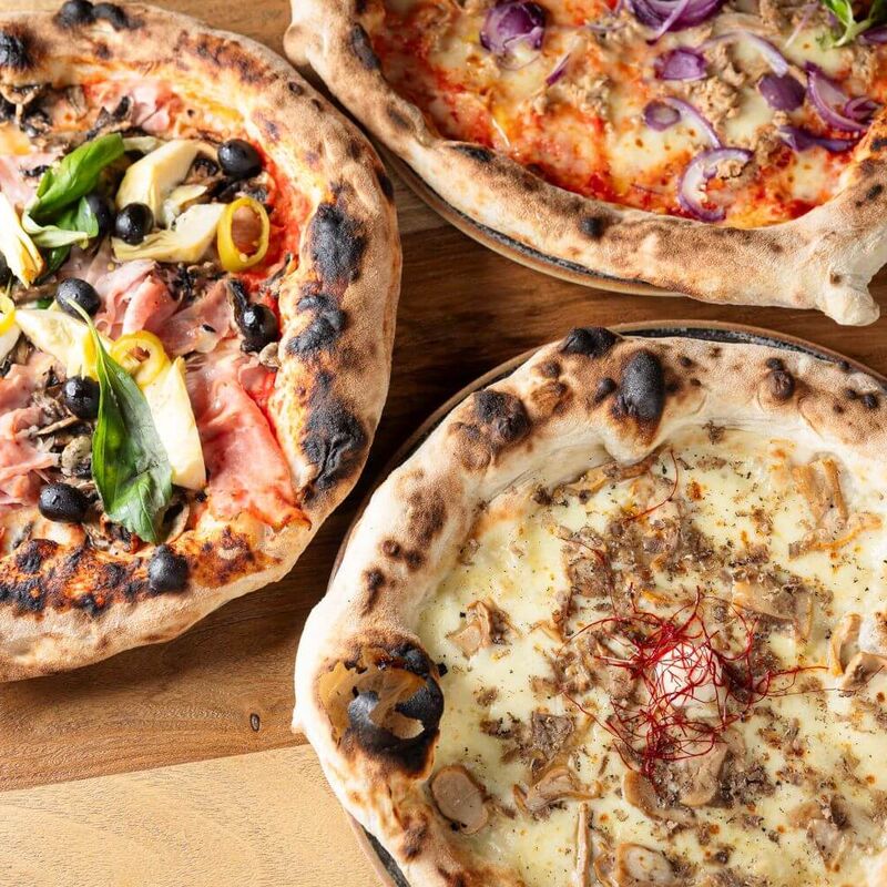 Drei neapolitanische frische Pizzen werden im mangia! Saalbach serviert.