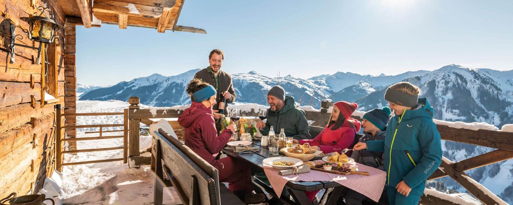 Family in a funny conversation with the landlord on the terrace of a ski hut