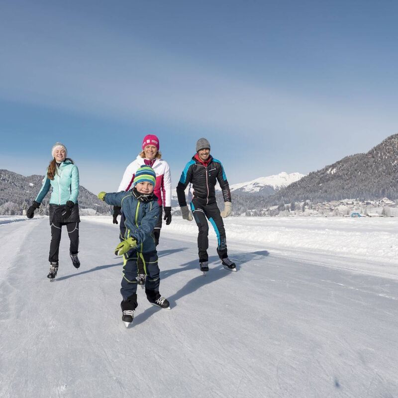 Familie läuft am Weissensee Eis, im Hintergrund die tief verschneite Landschaft.