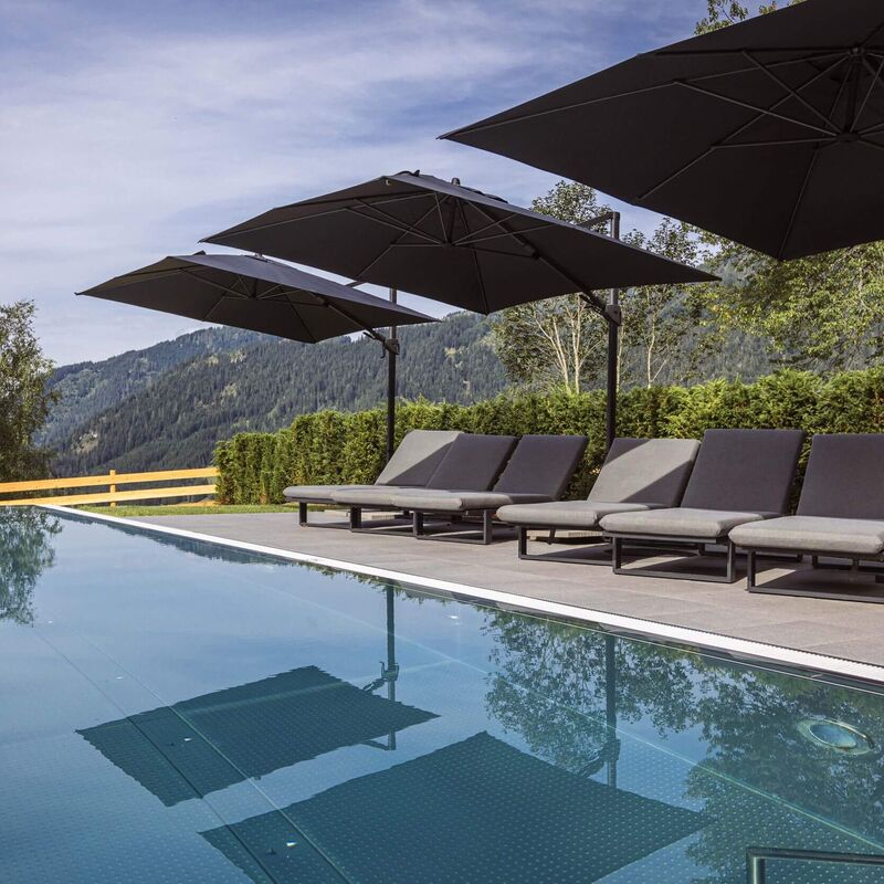 Moderner Infinitypool mit extrabreiten Sonnenliegen, weich gepolsterten Auflagen und großen Sonnenschirmen sowie traumhaftem Ausblick auf die grüne Berglandschaft im Salzburger Land.