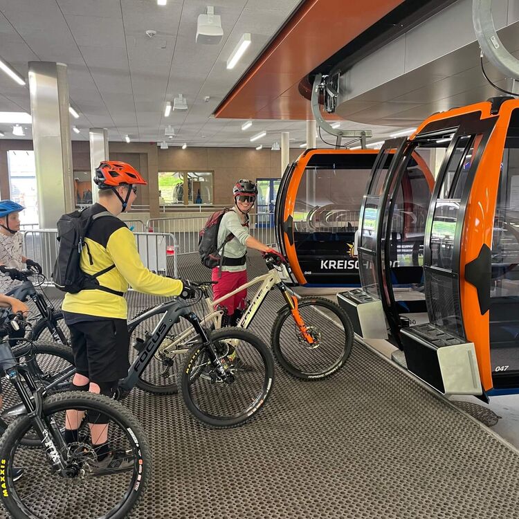 Menschen mit Mountainbikes stehen vor der Gondelbahn am Kreischberg und warten auf das Einsteigen.