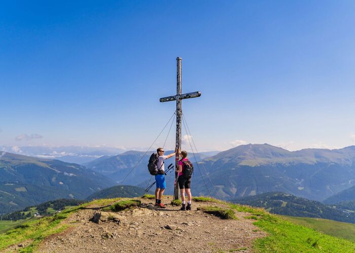 Zwei Wanderer am Gipfelkreuz in Kärnten bei Sonnenschein