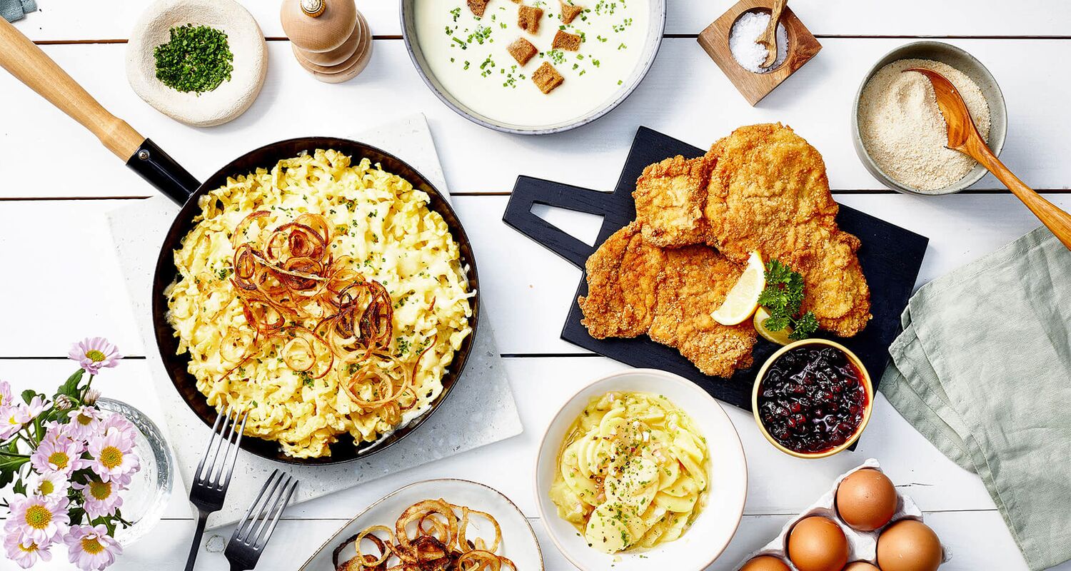 Deftige Zillertaler Speisen wie Käsespätzle, Schnitzel und traditionelle österreichische Hausmannskost auf rustikaler Tafel angerichtet. © Zillertal Tourismus / Kevin Ilse