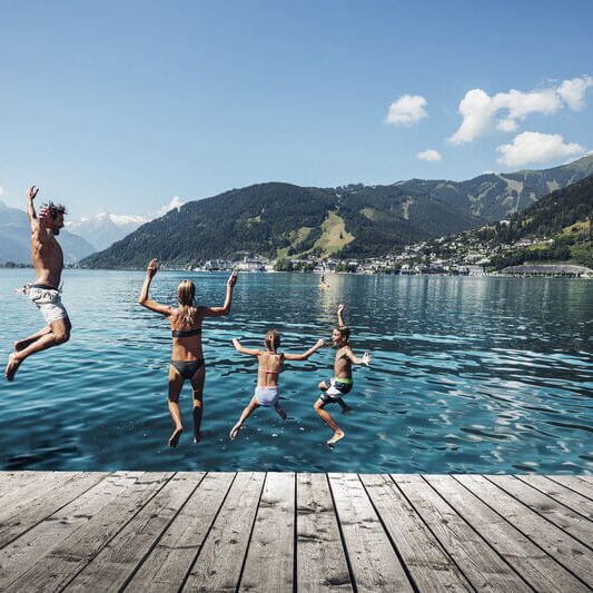 Familie springt in den Zeller See, im Hintergrund das Kitzsteinhorn und die Stadt Zell am See.