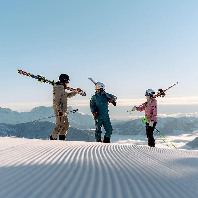 3 Skifahrer-Freunde stehen auf der frischen Piste oberhalb des Nebelmeers in der Sonne.