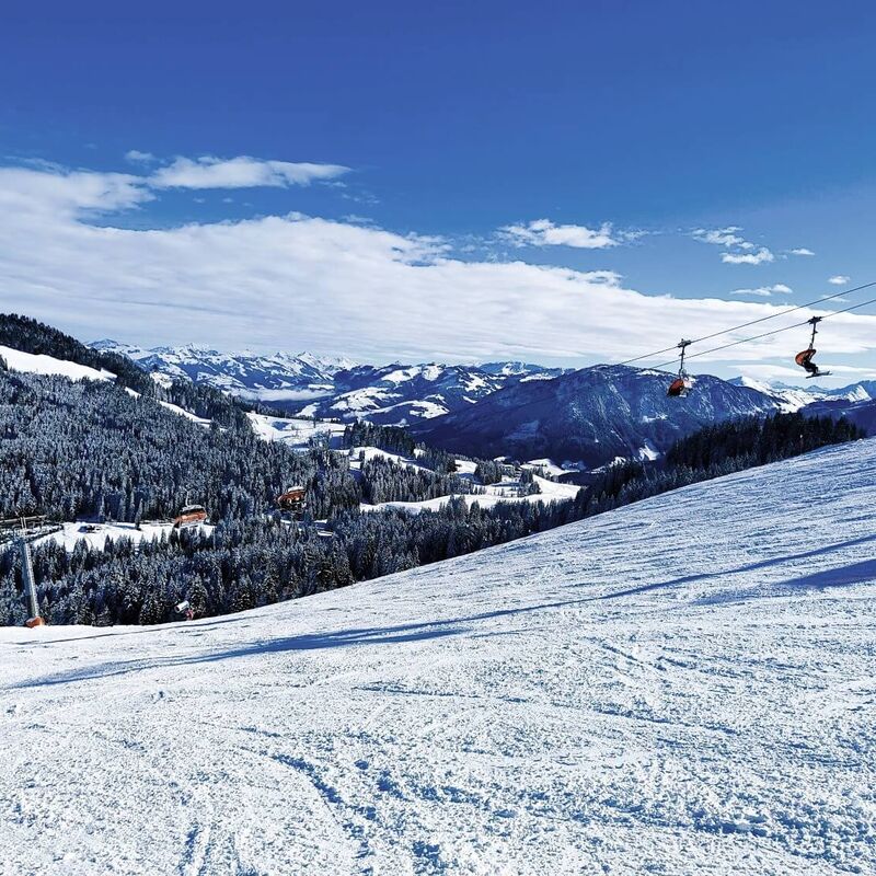 Moderne Sesselbahn schwebt über eine breite Carvingpiste.