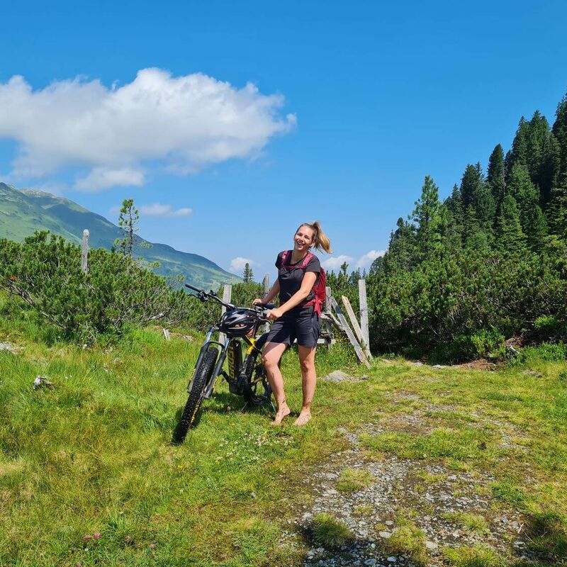 Bikerin in den Kitzbüheler Alpen schiebt ihr E-Bike ein Stück barfuß.