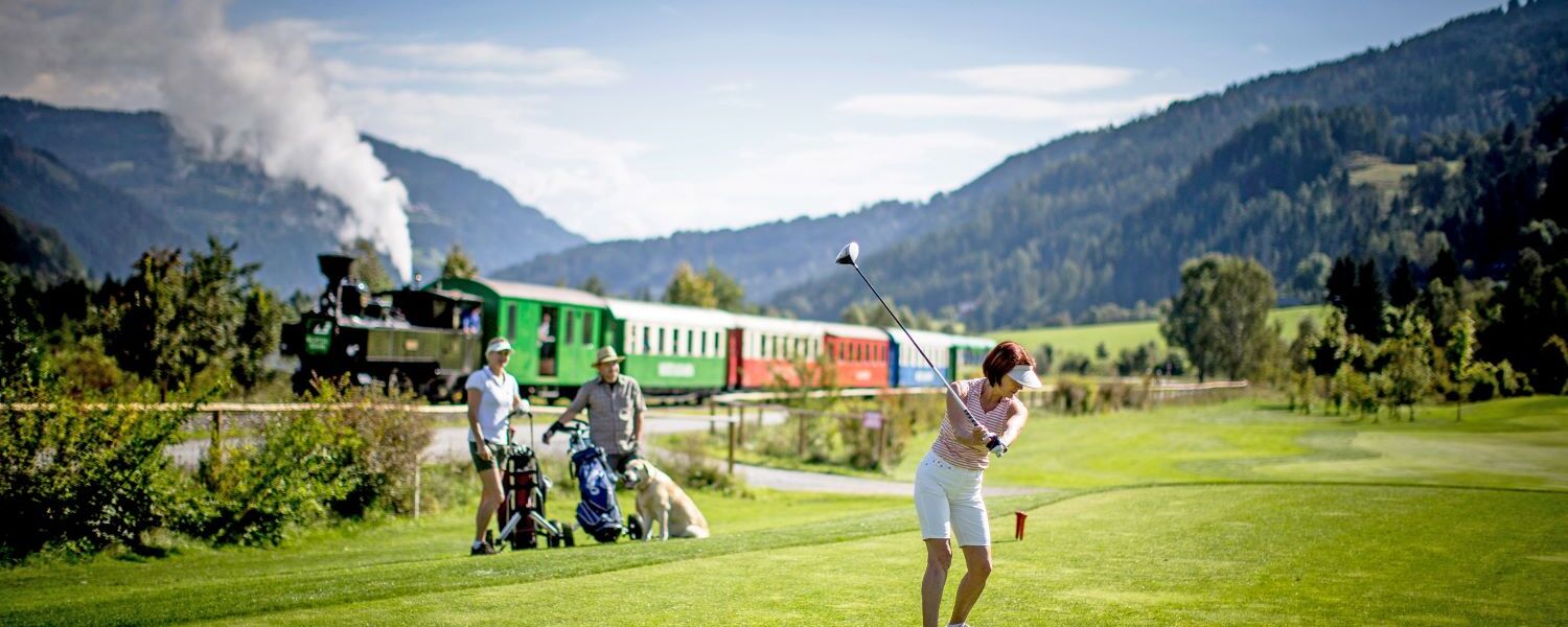 Golferin am Golfplatz, im Hintergrund die Murtalbahn