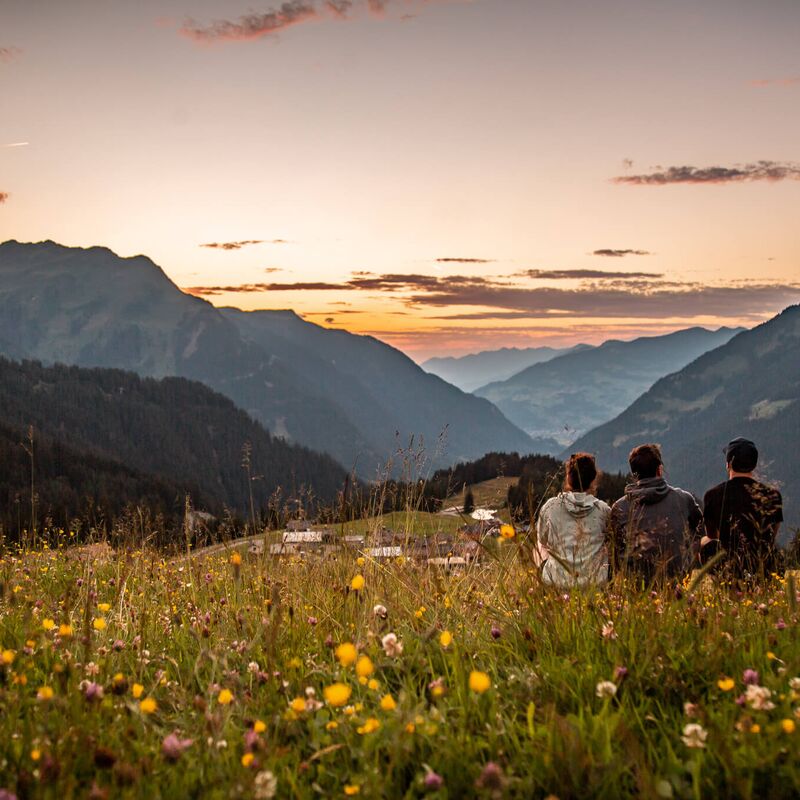 Urlauber entspannen auf einer Almwiese und genießen die besondere Lichtstimmung der Abenddämmerung inmitten imposanter Berglandschaft