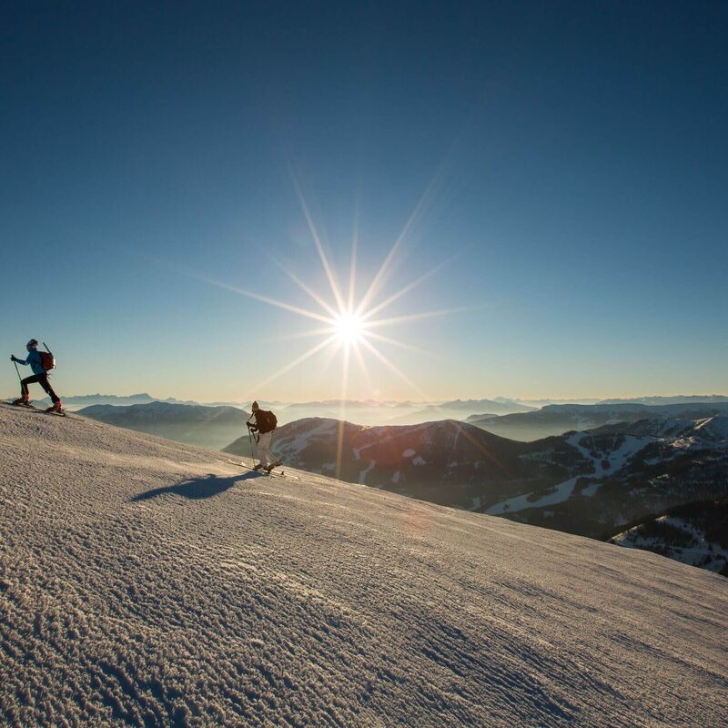 Zwei Skitourengeher steigen bei Sonnenaufgang durch die verschneiten Nockberge