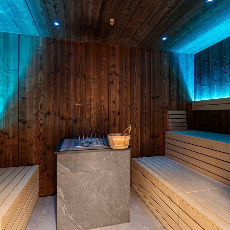 Sauna mit gemütlichen Holzbänken, Saunaofen aus Stein und entspannender Beleuchtung