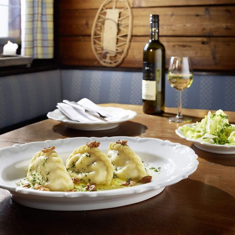 Gedeckter Holztisch mit Kärntner Kasnudeln, grünem Blattsalat und einer Flasche Weißwein