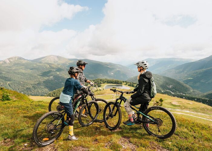 Drei Mountainbiker auf dem Flowtrail der Turracher Höhe in Kärnten mit Blick auf die Berglandschaft, die Strecke und den See